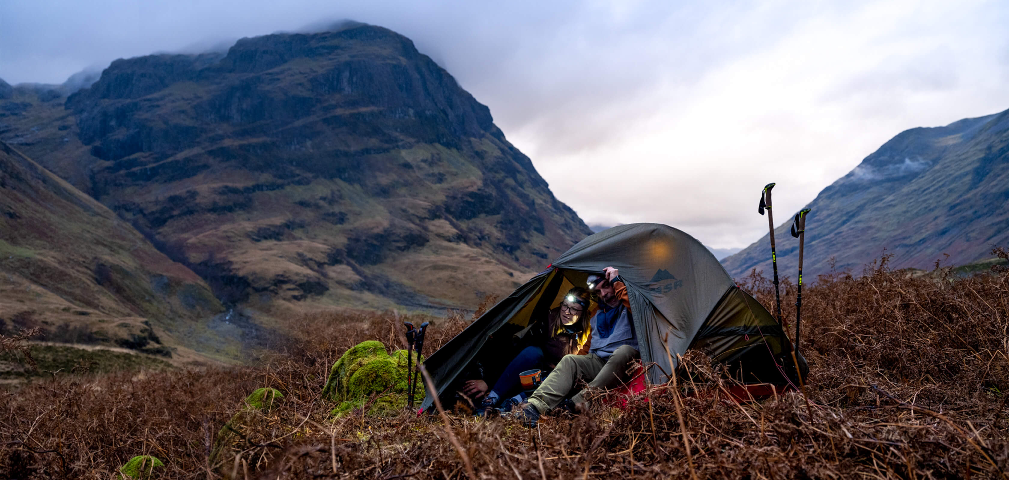 People are in a tent somewhere outdoors, surraunded by mountains.