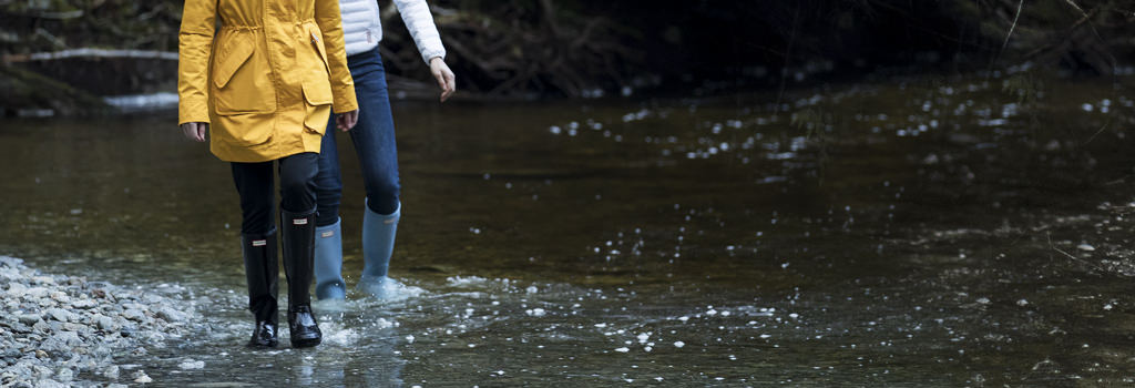 Two people wearing their wellie boots in the rain, walking through puddles