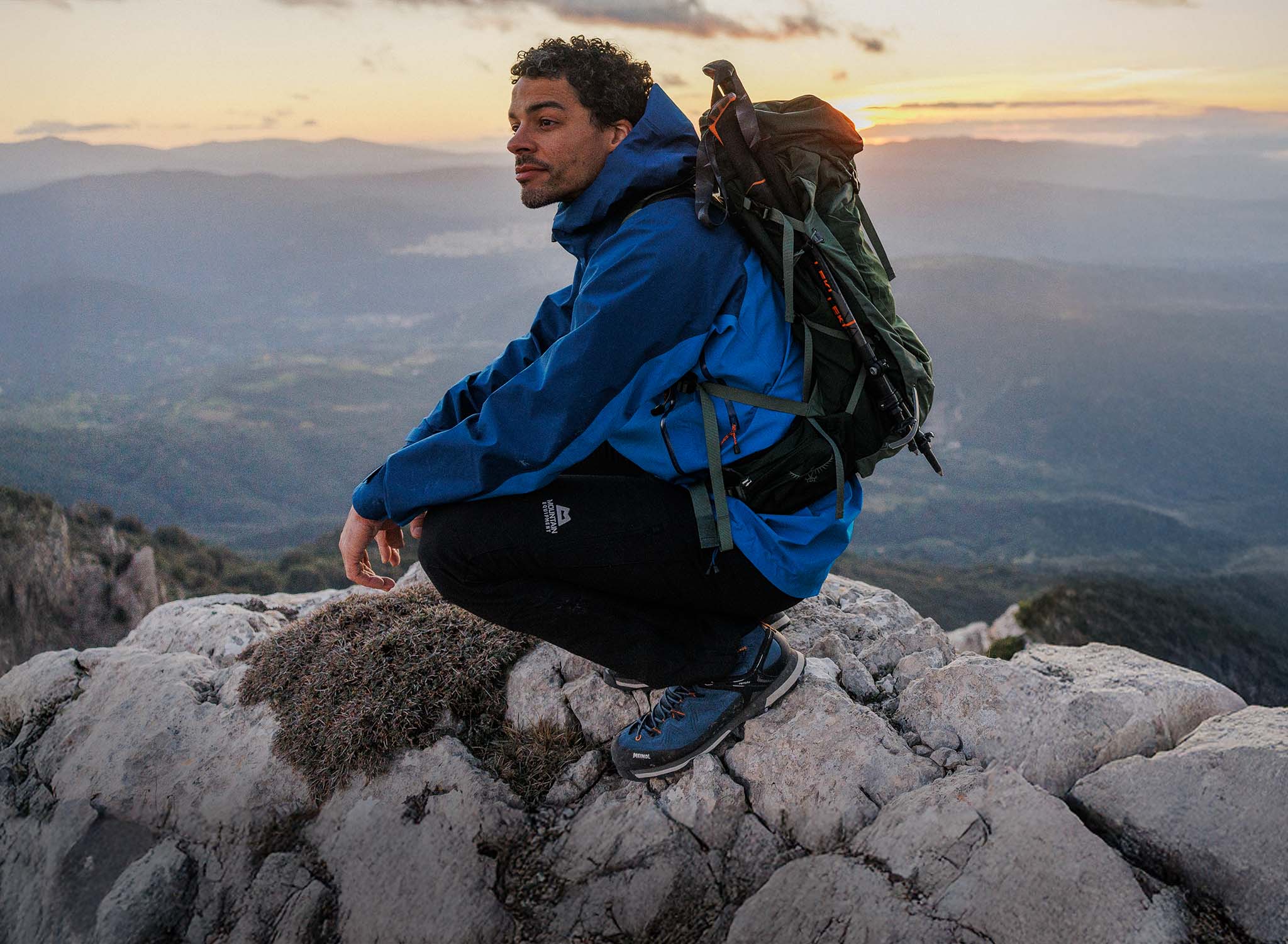 Man sitting on top of a rock, wearing a blue lightweight waterproof jacket