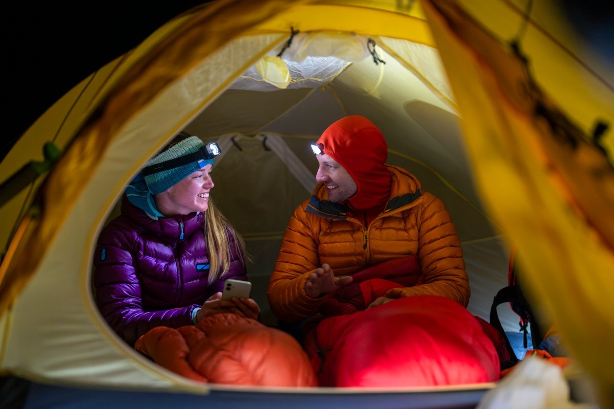 Two people talking in their tent at night, in their sleeping bags