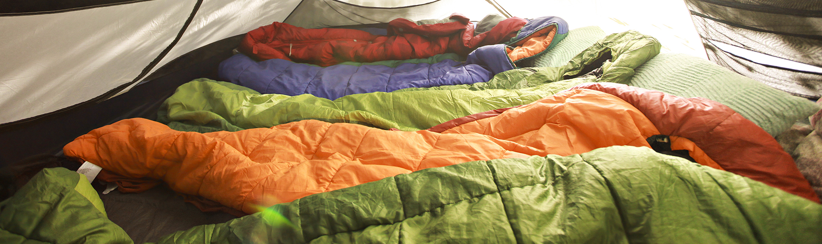 A row of brightly coloured sleeping bags within a tent